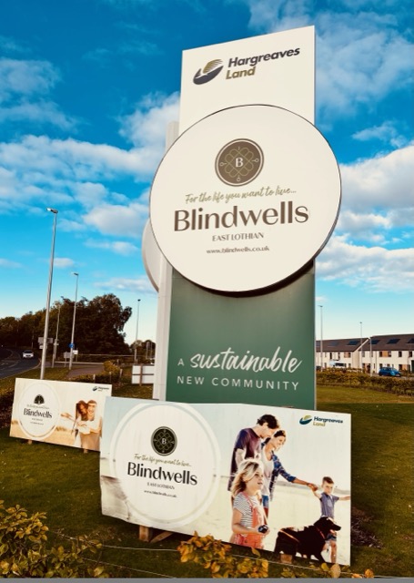Tall Blindwells entrance sign with Hargreaves Land branding and billboards beneath it