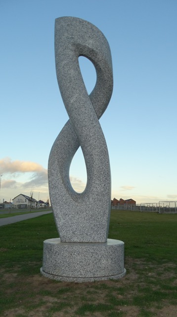 The granite sculpture at dusk with houses and the school in the distance