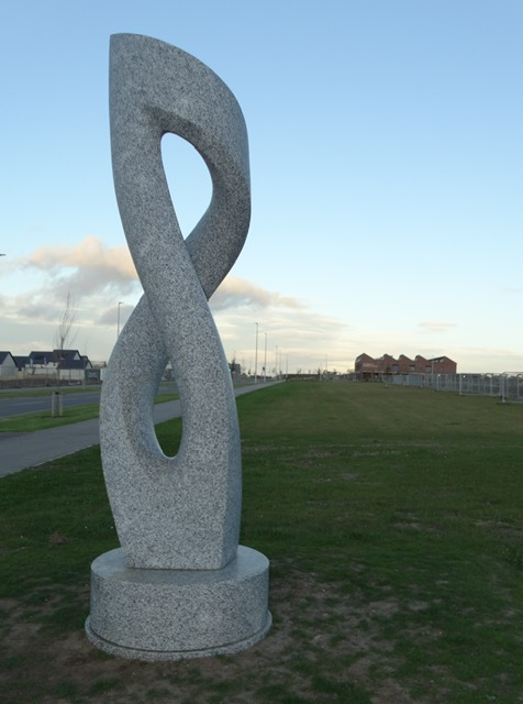 Twisting granite sculpture on a grass verge beside the path