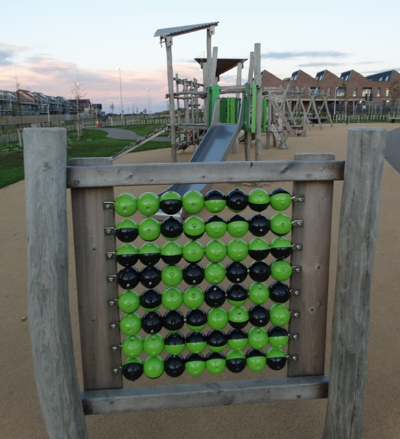 Wooden play panel with green and black beads like an abacus, with the play area behind