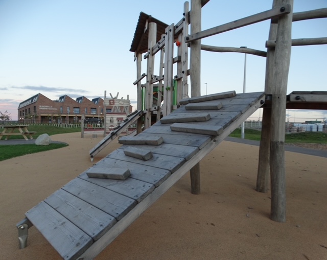 Wooden ramp and climbing frame in the playground, with new buildings behind